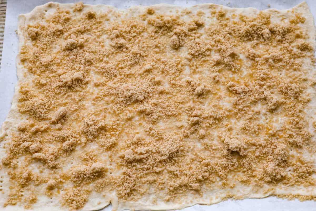 Maple Bacon Crack is as delicious and addicting as it sounds! It has flaky pastry dough drizzled in a sweet maple sauce and is loaded with crispy bacon pieces! It's the perfect sweet and salty snack! Overhead shot of brown sugar spread over the maple and crescent dough.
