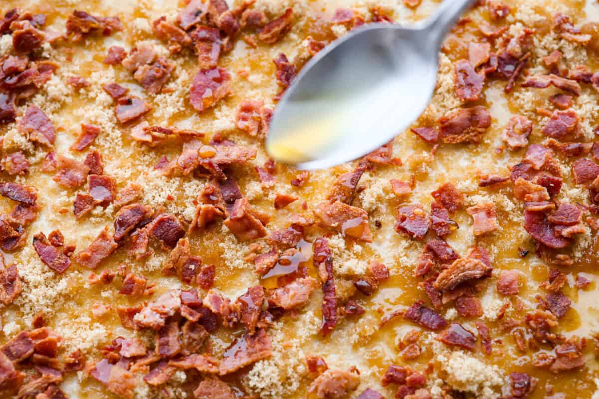 Maple Bacon Crack is as delicious and addicting as it sounds! It has flaky pastry dough drizzled in a sweet maple sauce and is loaded with crispy bacon pieces! It's the perfect sweet and salty snack! Close up shot of someone drizzling maple over the tope of everything.