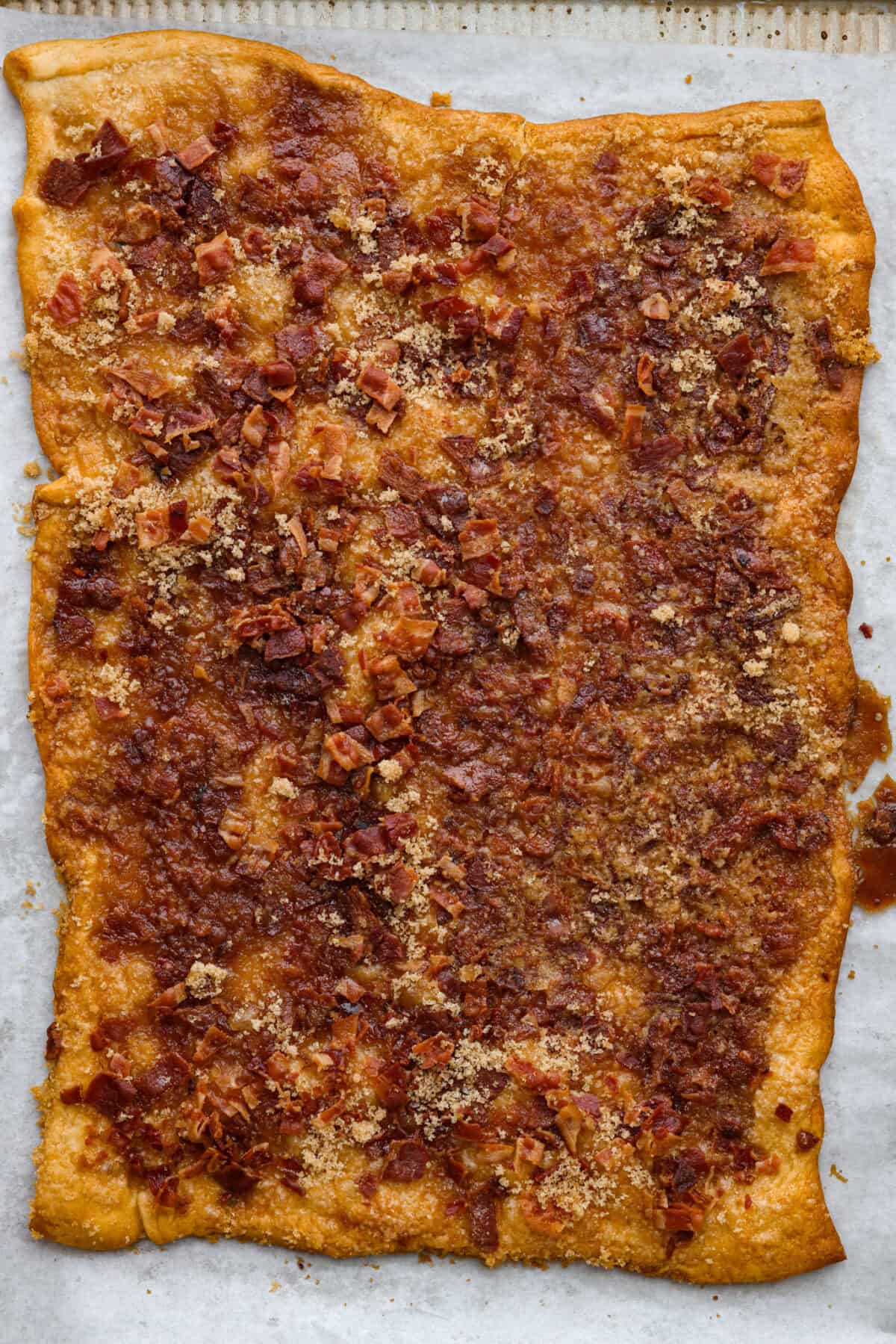 Maple Bacon Crack is as delicious and addicting as it sounds! It has flaky pastry dough drizzled in a sweet maple sauce and is loaded with crispy bacon pieces! It's the perfect sweet and salty snack! Overhead shot of a sheet of maple bacon crack.