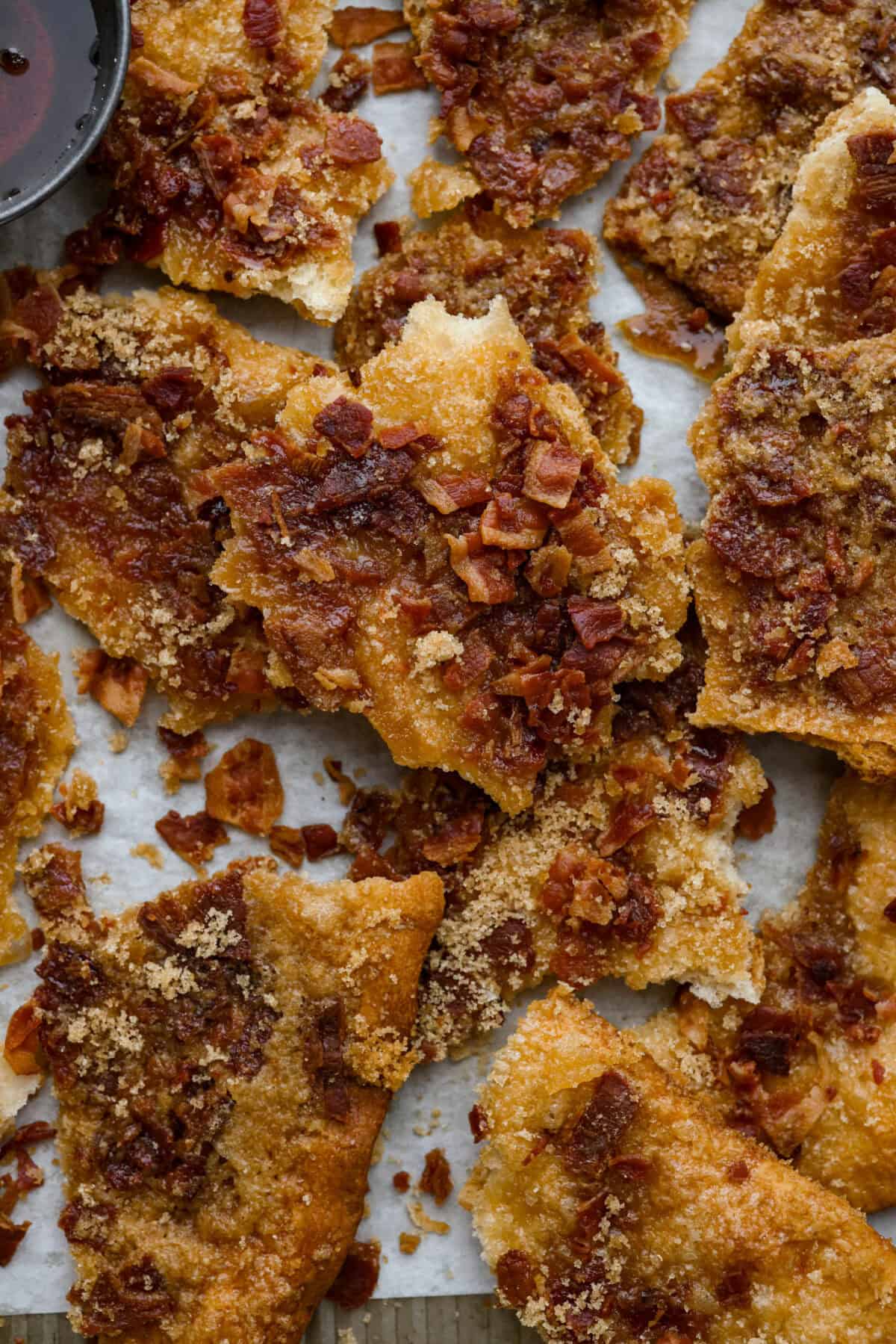 Maple Bacon Crack is as delicious and addicting as it sounds! It has flaky pastry dough drizzled in a sweet maple sauce and is loaded with crispy bacon pieces! It's the perfect sweet and salty snack! Close up shot of broken up pieces of maple bacon crack.