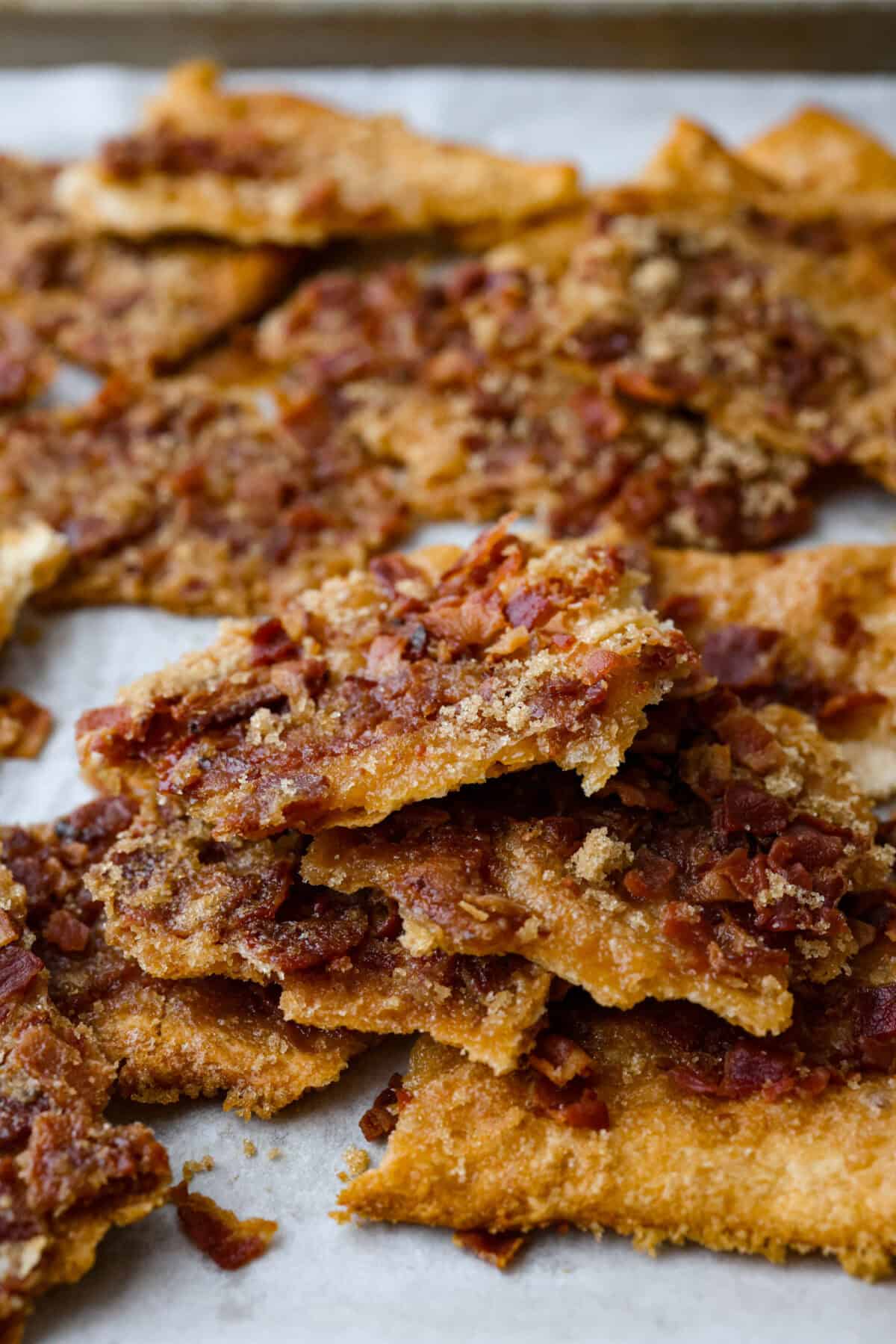 Maple Bacon Crack is as delicious and addicting as it sounds! It has flaky pastry dough drizzled in a sweet maple sauce and is loaded with crispy bacon pieces! It's the perfect sweet and salty snack! Angle shot of stacked pieces of maple bacon crack.