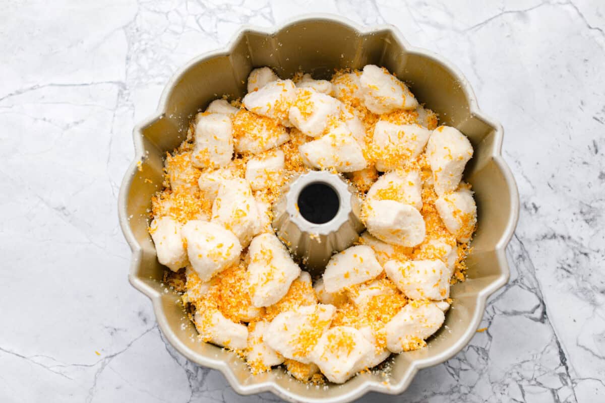 Overhead shot of biscuit pieces and sugar mixture in a greased bundt pan. 