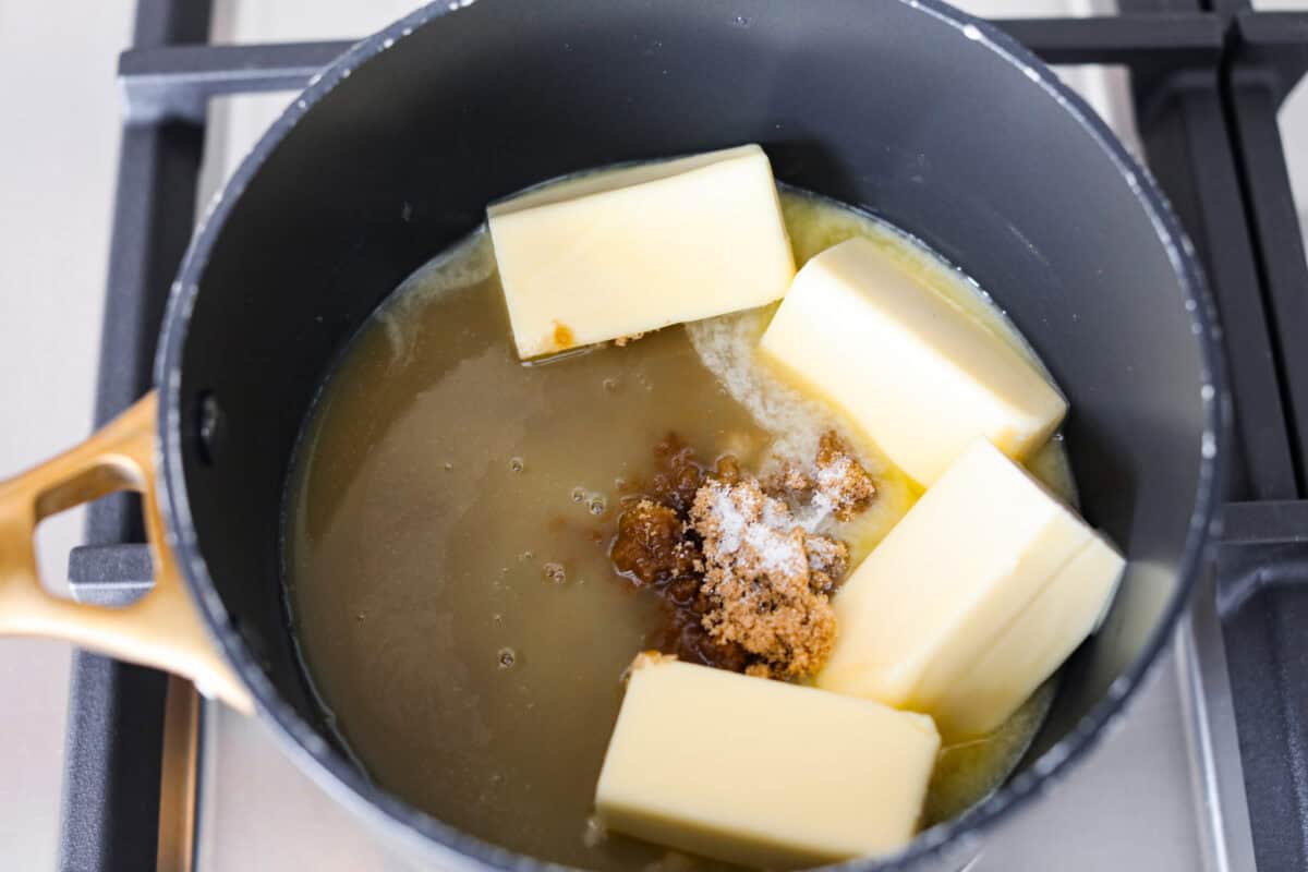 Overhead shot of butter, brown sugar and orange juice and salt in a pot on the stove. 