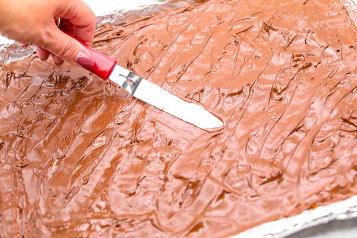 Angle shot of someone spreading the melted chocolate chips over the caramel mixture.