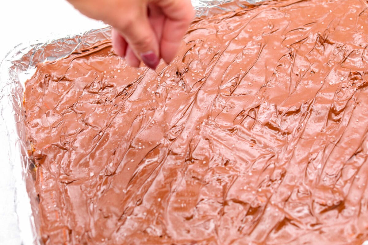 Angle shot of someone sprinkling flaky sea salt over the chocolate. 