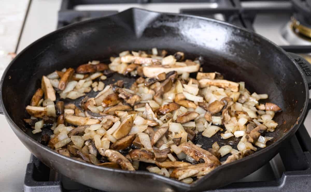 Angle shot of mushroom and onions cooking in the butter in a skillet.