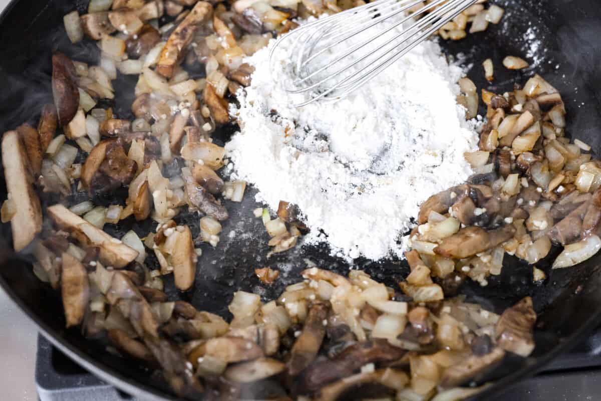 Angle shot of someone whisking flour into the mushroom butter and onion mixture. 