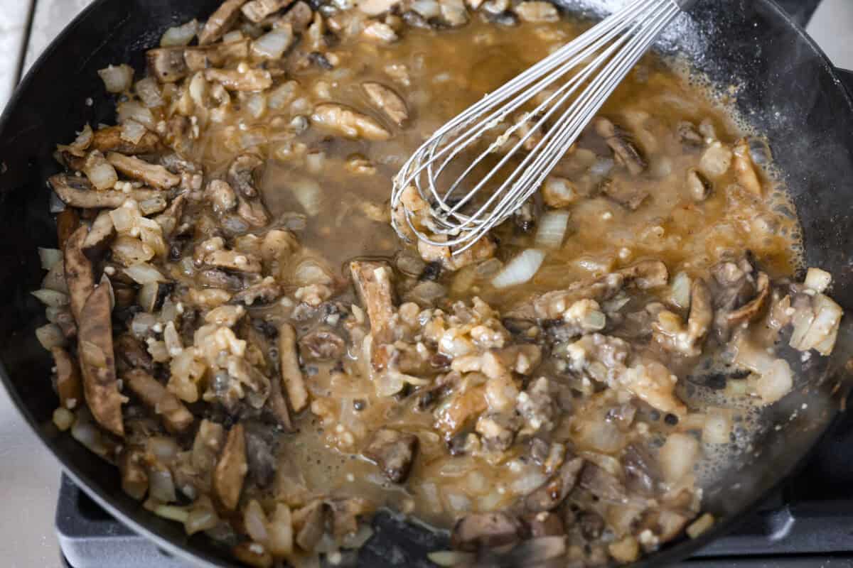 Overhead shot of someone whisking in beef broth into the vegetable roux. 