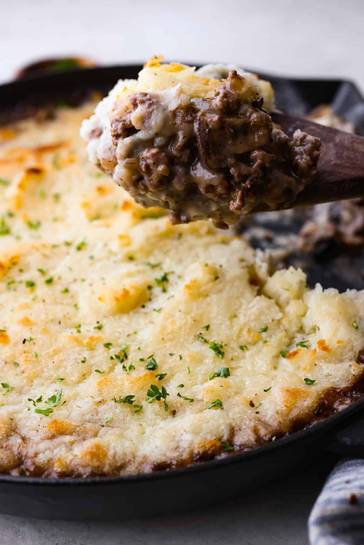 Side shot of someone lifting a scoop of the salisbury steak casserole out of the skillet. 