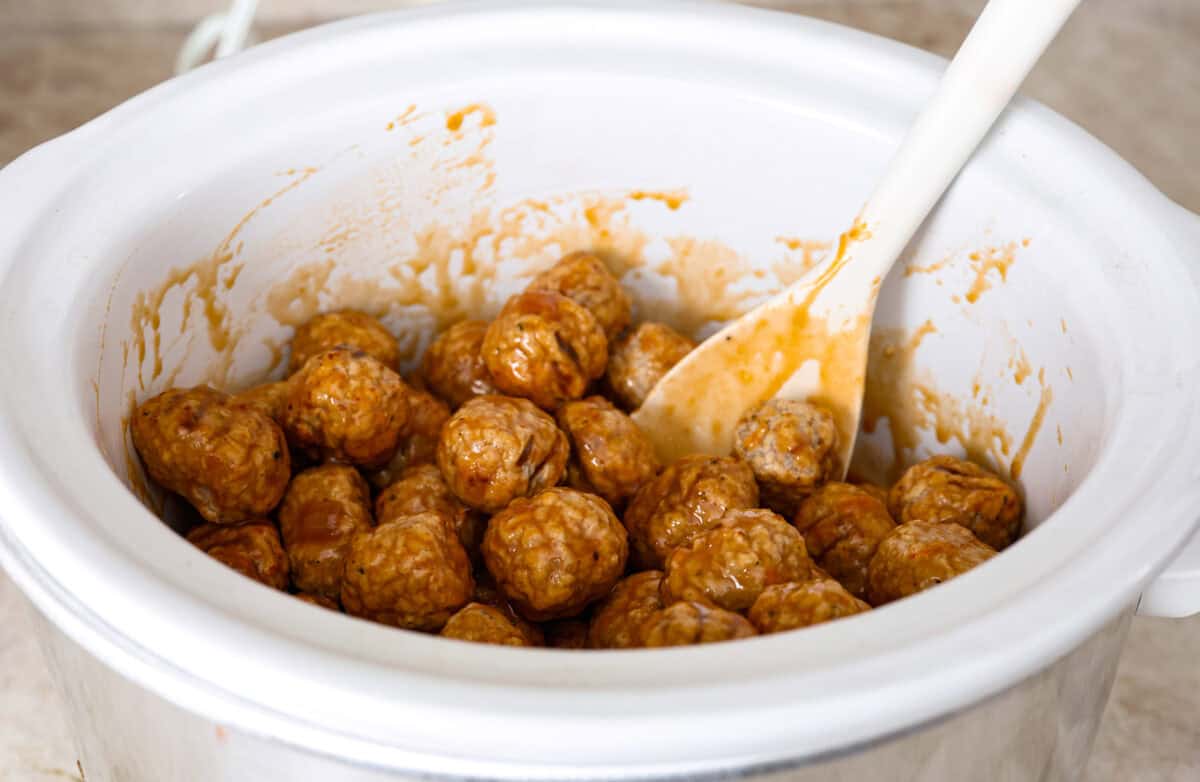 Tender, juicy Slow Cooker Honey Buffalo Meatballs are simmered in the most tantalizing sweet heat sauce that everyone goes crazy for! Perfect appetizer or delicious, easy meal! Angle shot of the meatballs mixed with the sauce in the crock pot.