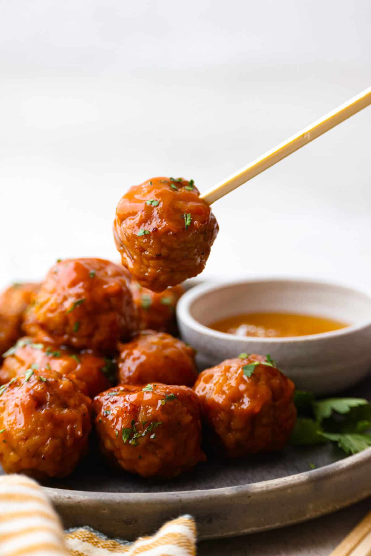 Tender, juicy Slow Cooker Honey Buffalo Meatballs are simmered in the most tantalizing sweet heat sauce that everyone goes crazy for! Perfect appetizer or delicious, easy meal! Side shot of plated slow cooker honey buffalo meatballs with one on a skewer.