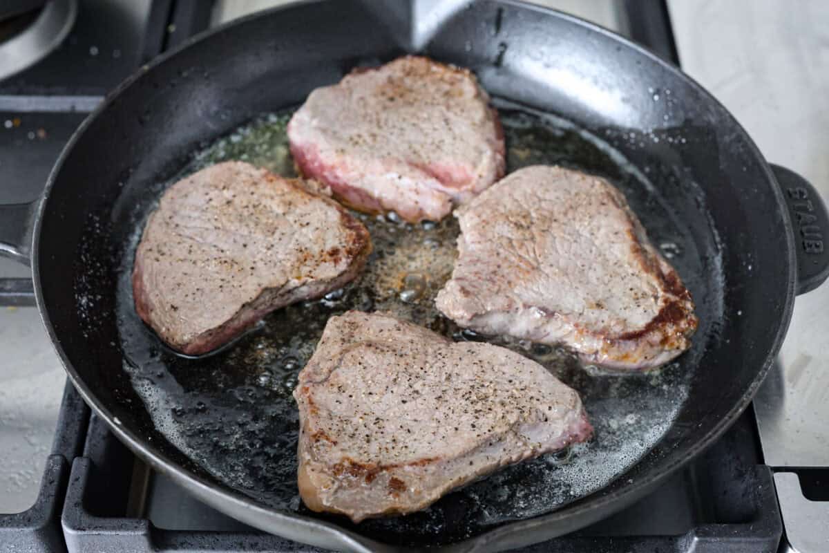 Craving Southern comfort food? This smothered steak is hearty, flavorful, and so satisfying. Perfectly cooked tender steak is covered in a rich, savory gravy that takes it to the next level. This steak is ready to enjoy in just 30 minutes! Angle shot of steaks cooking in a skillet.