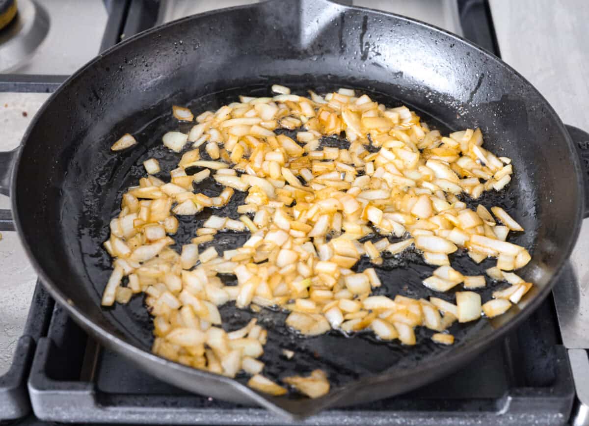 Craving Southern comfort food? This smothered steak is hearty, flavorful, and so satisfying. Perfectly cooked tender steak is covered in a rich, savory gravy that takes it to the next level. This steak is ready to enjoy in just 30 minutes! Angle shot of onions cooking in a skillet.