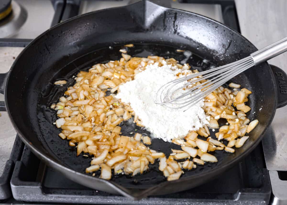 Craving Southern comfort food? This smothered steak is hearty, flavorful, and so satisfying. Perfectly cooked tender steak is covered in a rich, savory gravy that takes it to the next level. This steak is ready to enjoy in just 30 minutes! Angle shot of flour being stirred into the cooked onions.