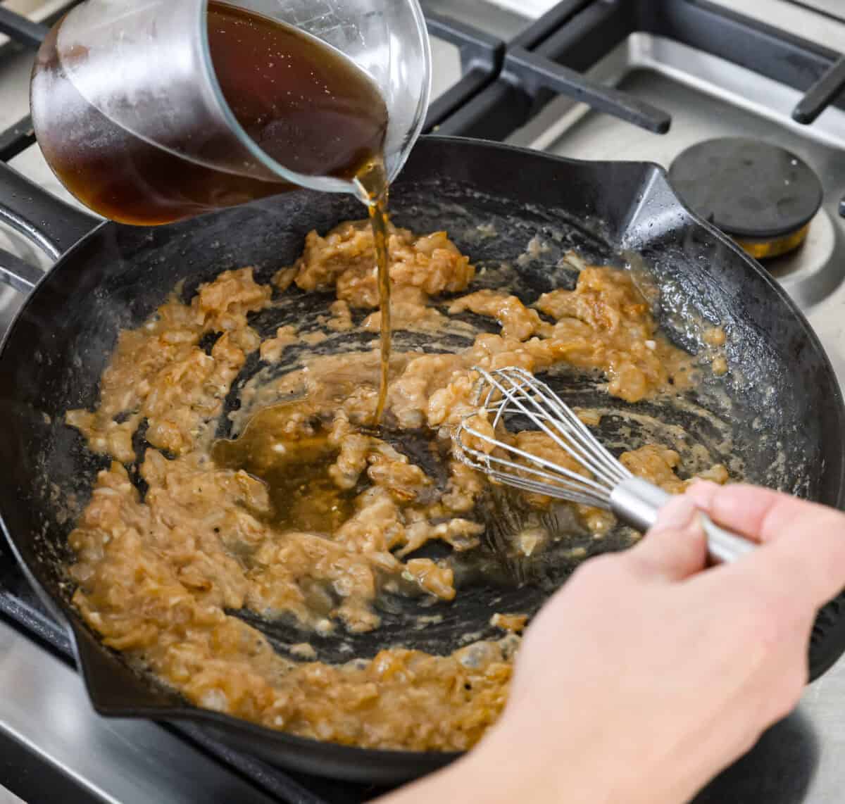 Craving Southern comfort food? This smothered steak is hearty, flavorful, and so satisfying. Perfectly cooked tender steak is covered in a rich, savory gravy that takes it to the next level. This steak is ready to enjoy in just 30 minutes! Angles hot of someone pouring beef broth into the flour and onion mixture in the skillet.