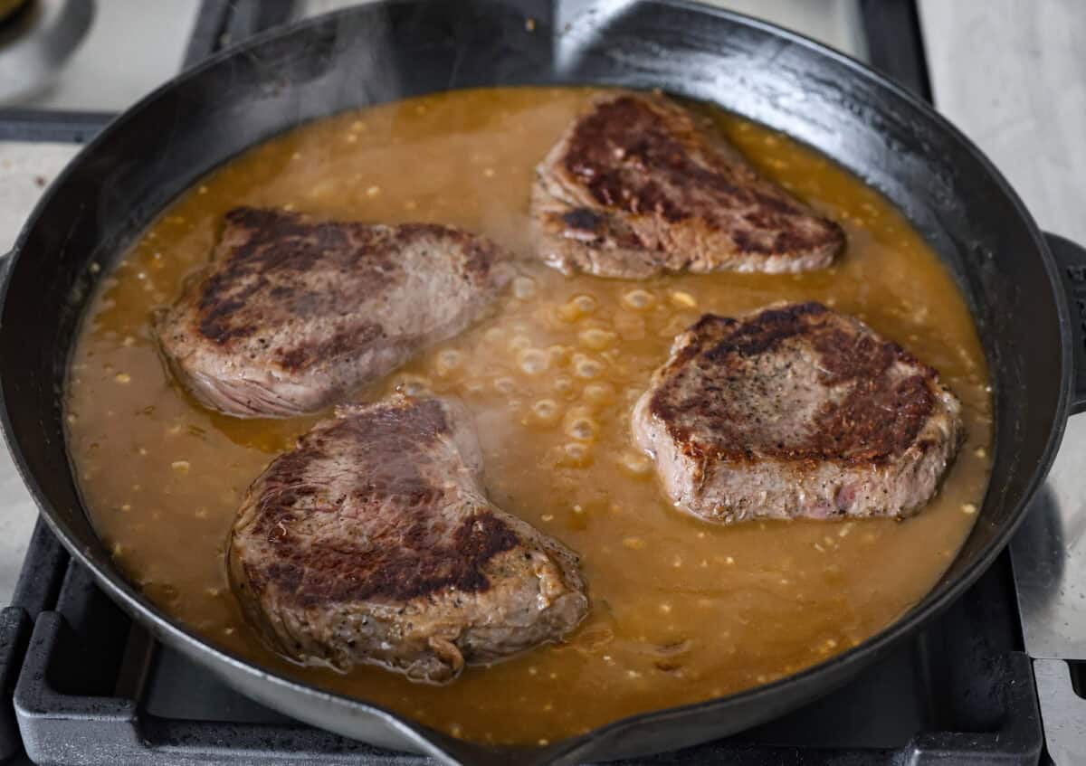 Craving Southern comfort food? This smothered steak is hearty, flavorful, and so satisfying. Perfectly cooked tender steak is covered in a rich, savory gravy that takes it to the next level. This steak is ready to enjoy in just 30 minutes! Angle shot of the steaks back in the gravy in the skillet.