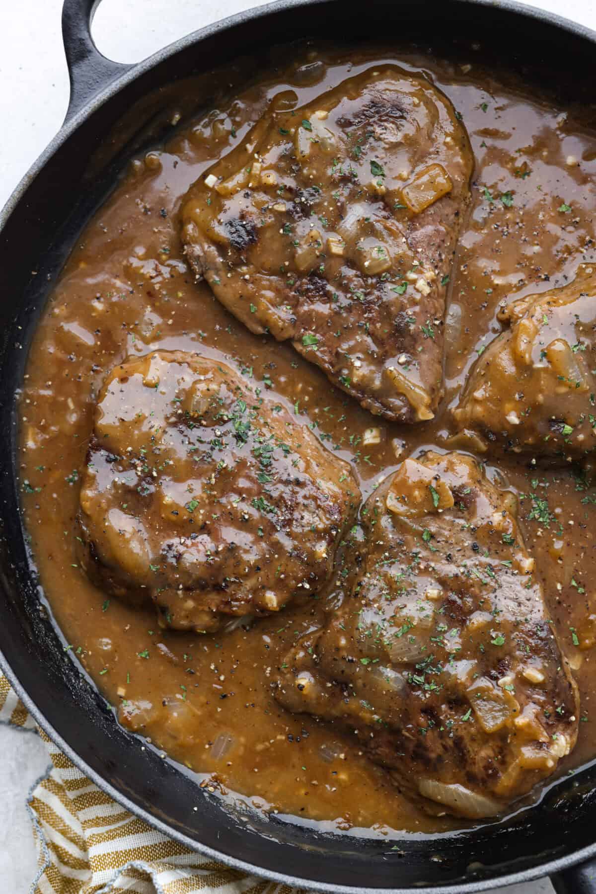 Craving Southern comfort food? This smothered steak is hearty, flavorful, and so satisfying. Perfectly cooked tender steak is covered in a rich, savory gravy that takes it to the next level. This steak is ready to enjoy in just 30 minutes! Overhead shot of smothered steak in a skillet.