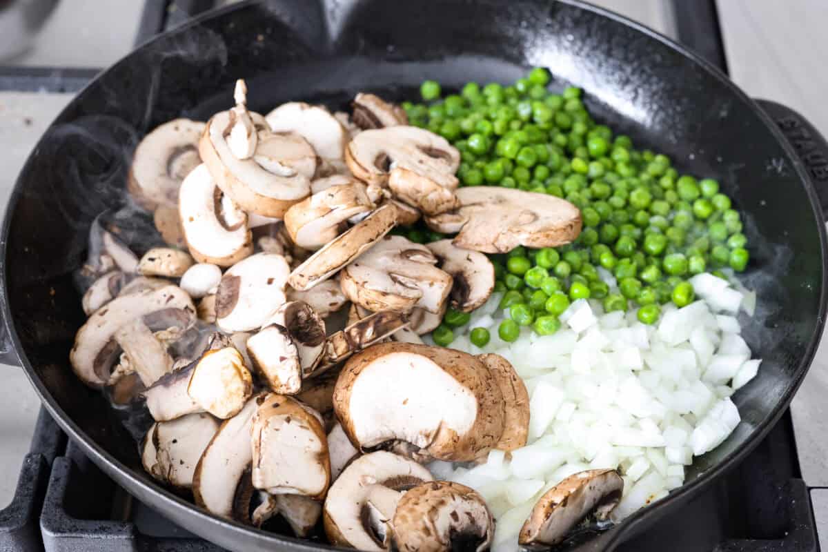 Chicken a la king is a timeless recipe that’s perfect for cozy dinners! This classic dish features tender chicken and veggies in a rich, creamy gravy-like sauce loaded with savory flavor. Overhead shot of the butter, mushrooms, onion and peas cooking in a skillet.