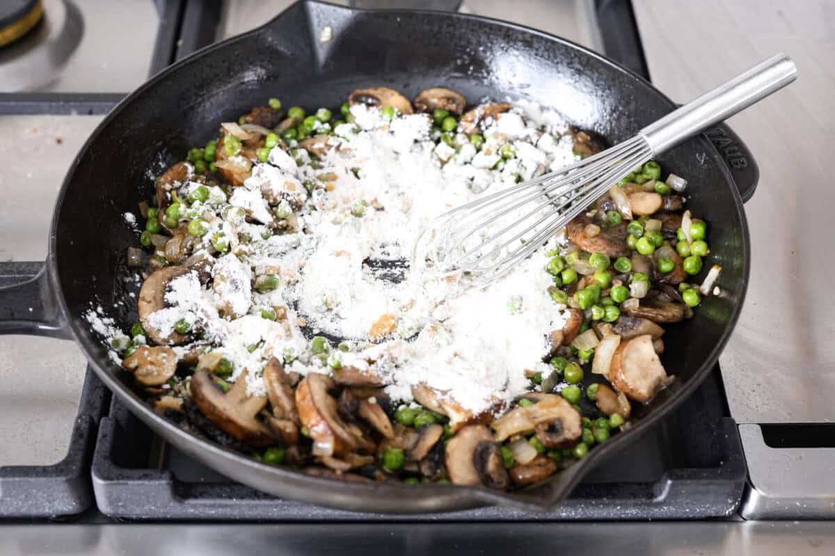 Chicken a la king is a timeless recipe that’s perfect for cozy dinners! This classic dish features tender chicken and veggies in a rich, creamy gravy-like sauce loaded with savory flavor. Angle shot of flour being whisked into the veggies and garlic on the skillet.