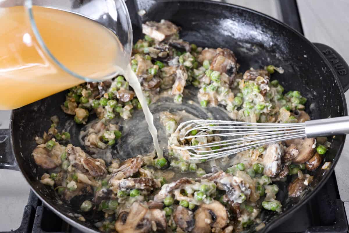 Chicken a la king is a timeless recipe that’s perfect for cozy dinners! This classic dish features tender chicken and veggies in a rich, creamy gravy-like sauce loaded with savory flavor. Angle shot of someone pouring in the chicken broth into the flour and veggie mixture.