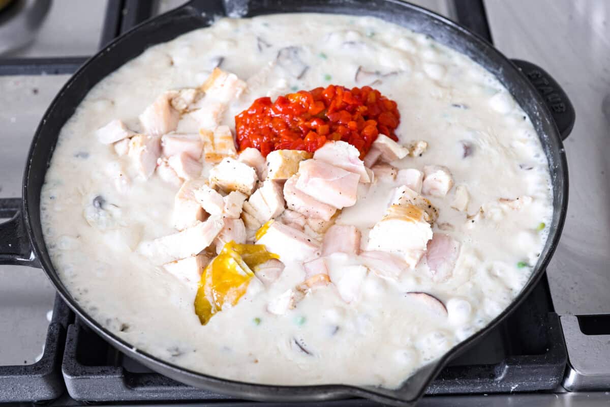 Chicken a la king is a timeless recipe that’s perfect for cozy dinners! This classic dish features tender chicken and veggies in a rich, creamy gravy-like sauce loaded with savory flavor. Angle shot of the pimentos, chicken, vinegar and bullion being added into the chicken a la kings sauce in the skillet.