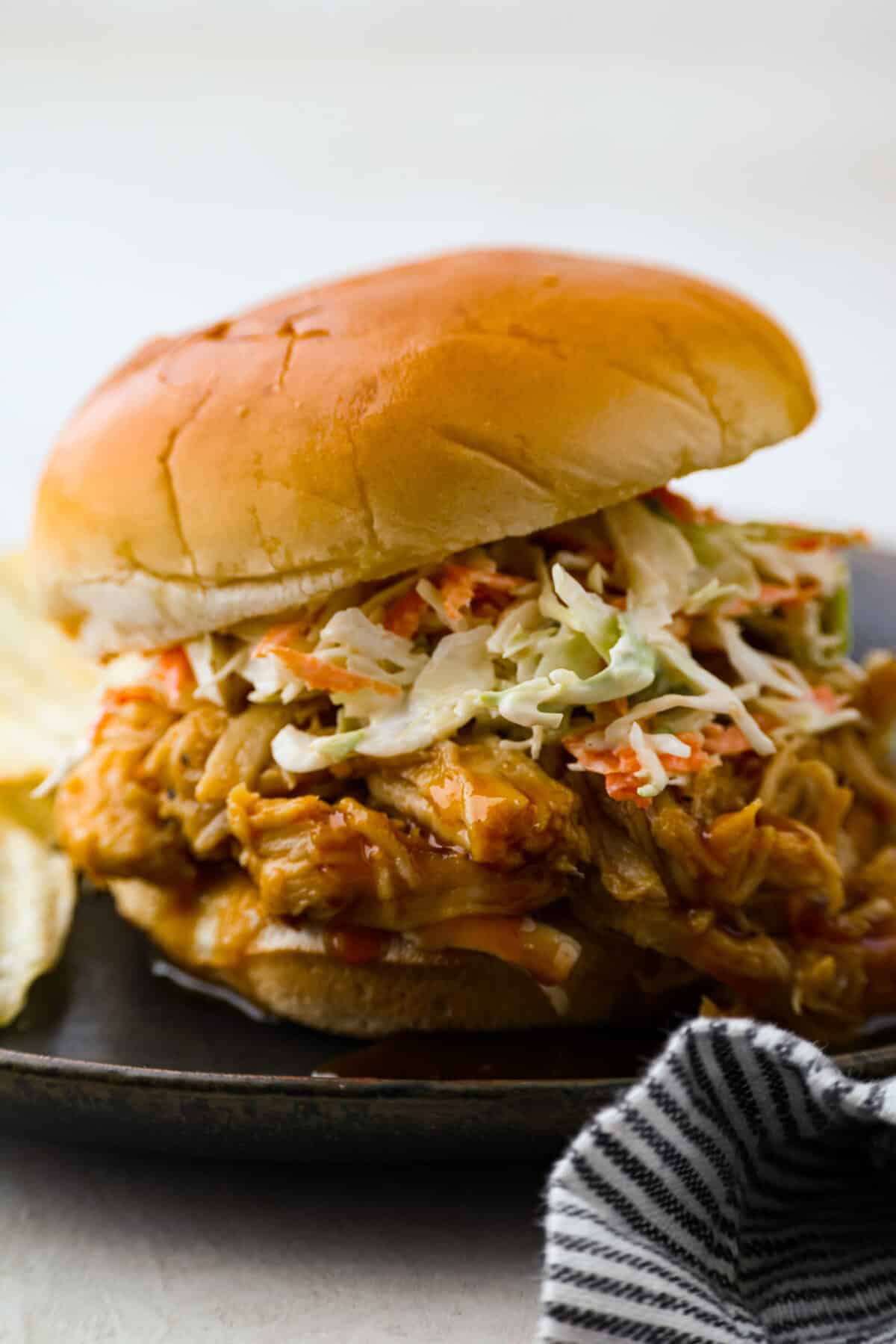 Slow cooker shredded BBQ chicken is a simple, zesty, and flavorful chicken. It can go in pasta dishes, over potatoes, in sandwiches, or in tortillas. This recipe is extremely versatile, tasty, and perfect for any time of year! Side shot of sandwich with slow cooker shredded bbq chicken and coleslaw.