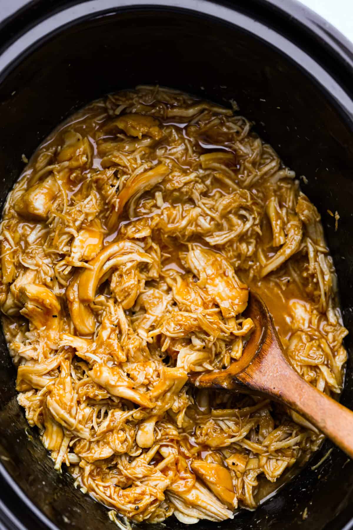 Slow cooker shredded BBQ chicken is a simple, zesty, and flavorful chicken. It can go in pasta dishes, over potatoes, in sandwiches, or in tortillas. This recipe is extremely versatile, tasty, and perfect for any time of year! Overhead shot of slow cooker shredded BBQ chicken in the crockpot.