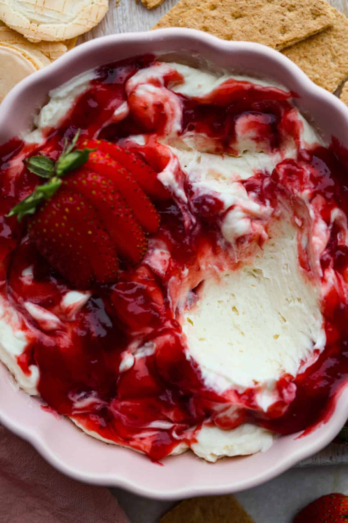 Strawberry cheesecake dip is an irresistible treat that tastes just like the classic but in a fun dip form! Whip it up in just 5 minutes! It's so good with graham crackers, fresh fruit, and cookies for a sweet, crowd-pleasing snack! Close up shot of strawberry cheesecake dip in a serving dish.