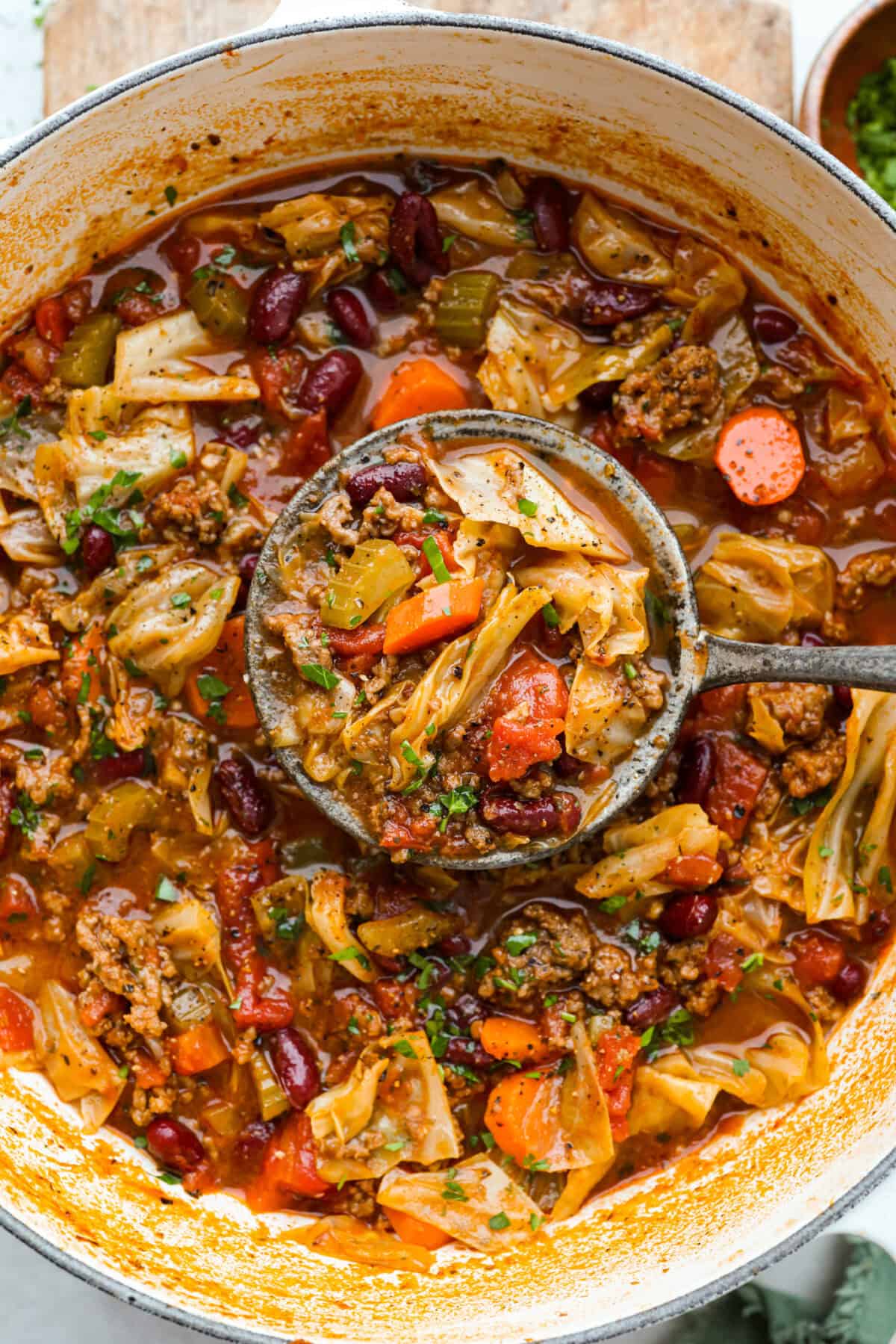 Beef and Cabbage soup is filled with seasoned ground beef, cabbage, carrots, celery, kidney beans, and diced tomatoes. It is hearty, delicious, and full of flavor! This is a great soup to serve on a cold day or to help you get in the spirit of St. Patrick's Day while keeping your nutrition goals in check. Overhead shot of beef and cabbage soup in a large pot with a ladle full of soup.
