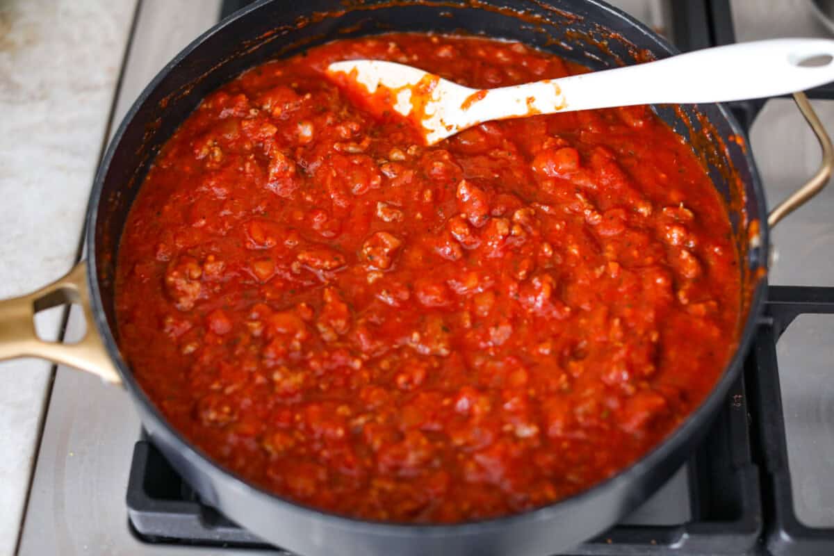 Baked spaghetti is the ultimate comfort food, with noodles that soak up all of the rich sauce as they finish cooking, making every bite extra flavorful. Plus, it’s a lifesaver on busy days. You can prep it ahead, pop it in the oven, and still have a cozy, home-cooked meal without the stress! Overhead shot of marinara added to the meat and onion mixture.