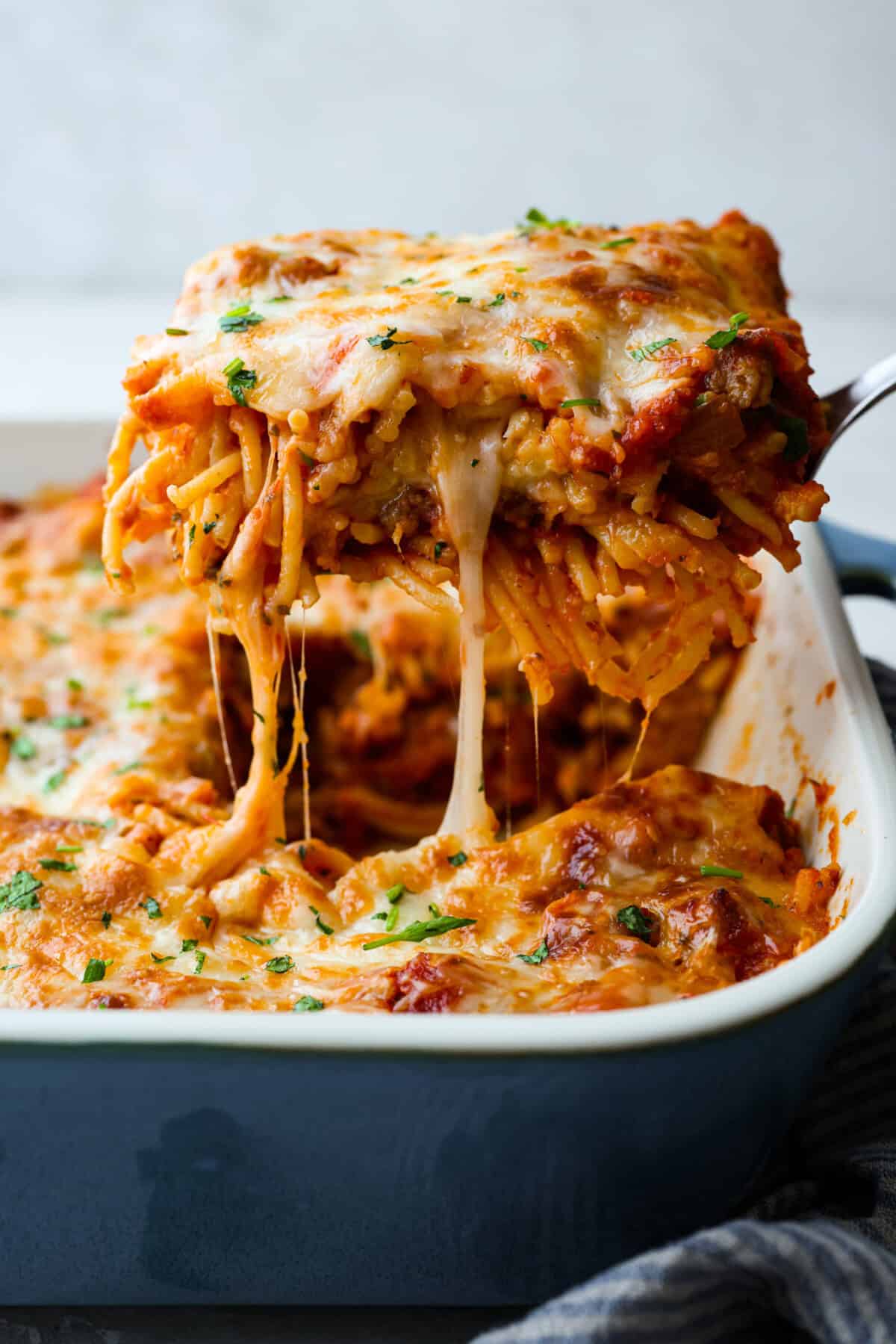 Baked spaghetti is the ultimate comfort food, with noodles that soak up all of the rich sauce as they finish cooking, making every bite extra flavorful. Plus, it’s a lifesaver on busy days. You can prep it ahead, pop it in the oven, and still have a cozy, home-cooked meal without the stress! Side shot of someone lifting a piece of baked spaghetti out of the pan.