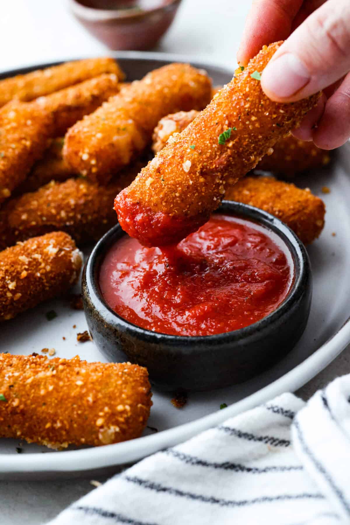 The secret to perfect mozzarella sticks comes down to three key steps: using the right mozzarella, double breading for a sturdy crust, and fully freezing them before frying. I’ve broken down these expert tips below! Someone dipping a mozzarella stick into marinara sauce.