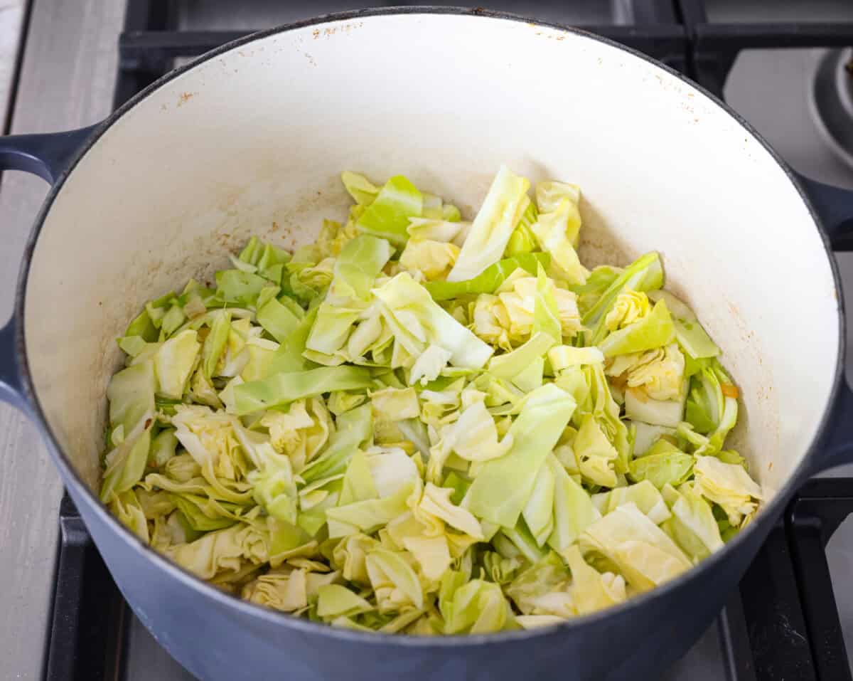 This colcannon soup is a creamy, luscious soup inspired by the traditional Irish dish that is made with potatoes, cabbage, kale, butter, and cream. This would be a great recipe to start a St. Patrick's Day tradition with your family. Overhead shot of cabbage added to the butter onions and garlic.