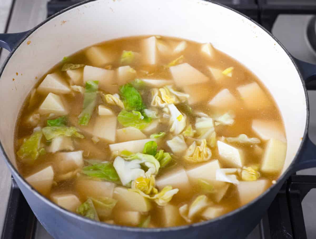 This colcannon soup is a creamy, luscious soup inspired by the traditional Irish dish that is made with potatoes, cabbage, kale, butter, and cream. This would be a great recipe to start a St. Patrick's Day tradition with your family. Overhead shot of potatoes, and broth added to the pot.