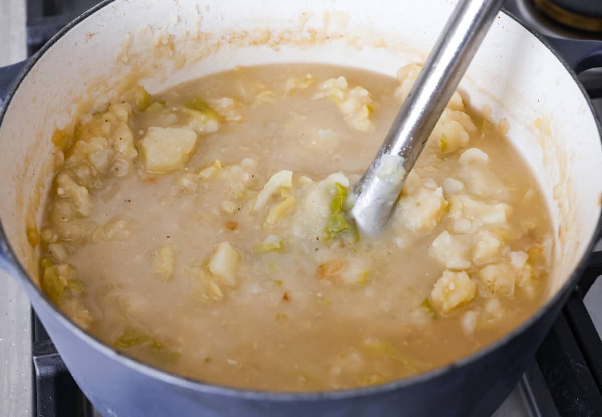 This colcannon soup is a creamy, luscious soup inspired by the traditional Irish dish that is made with potatoes, cabbage, kale, butter, and cream. This would be a great recipe to start a St. Patrick's Day tradition with your family. Angle shot of someone using an immersion blender to blend up the potatoes in the broth.