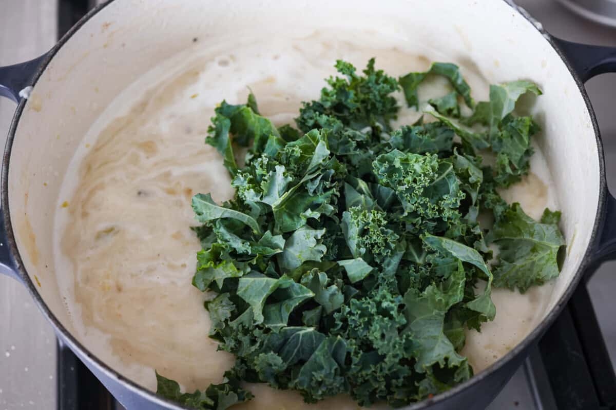 This colcannon soup is a creamy, luscious soup inspired by the traditional Irish dish that is made with potatoes, cabbage, kale, butter, and cream. This would be a great recipe to start a St. Patrick's Day tradition with your family. Close up shot of the kale and half and half being added to the colcannon soup.
