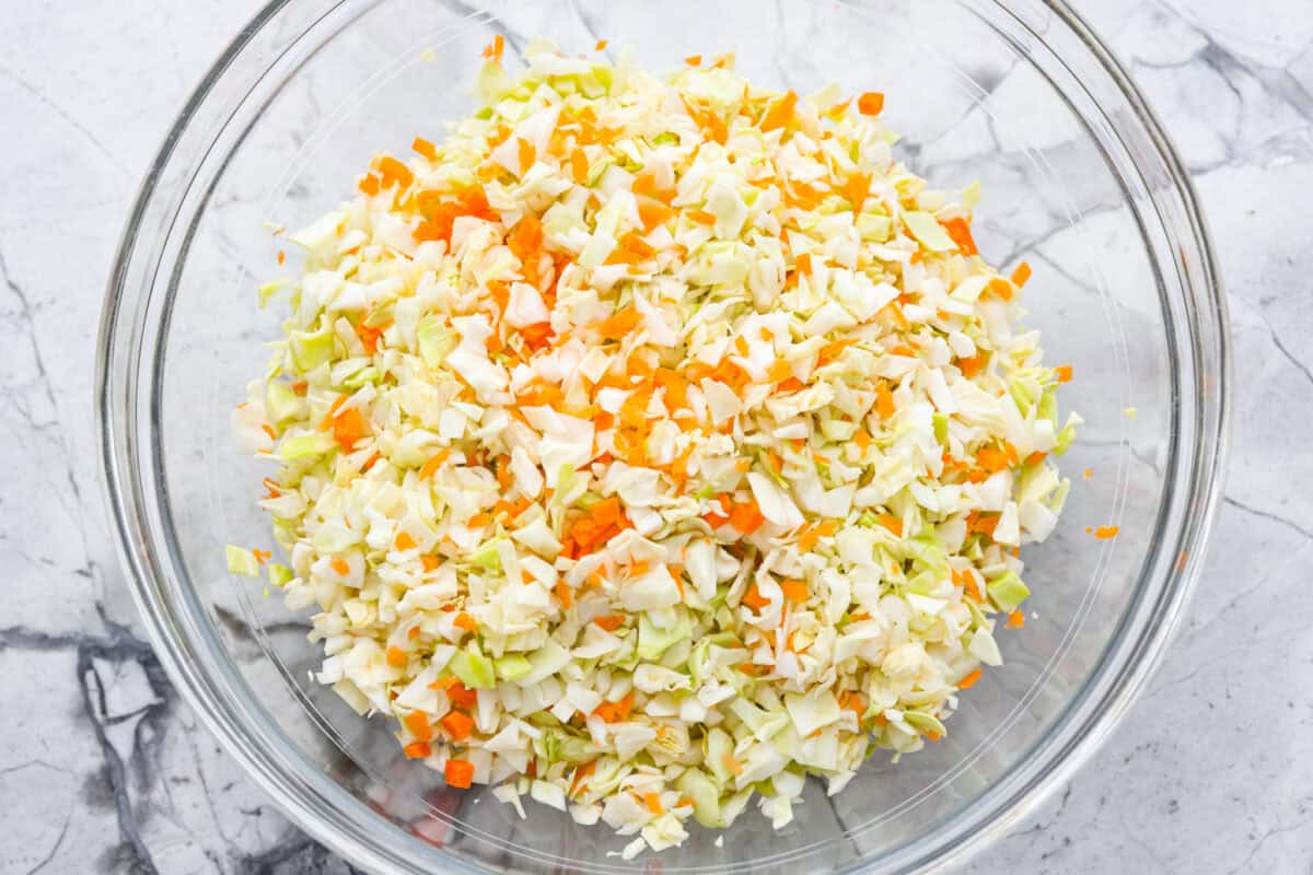 My Copycat KFC Coleslaw is so spot-on, you’ll think it’s the real deal! Crunchy, creamy, tangy, and perfect for any BBQ, everyone will want the recipe! Overhead shot of chopped carrots and cabbage in a mixing bowl.