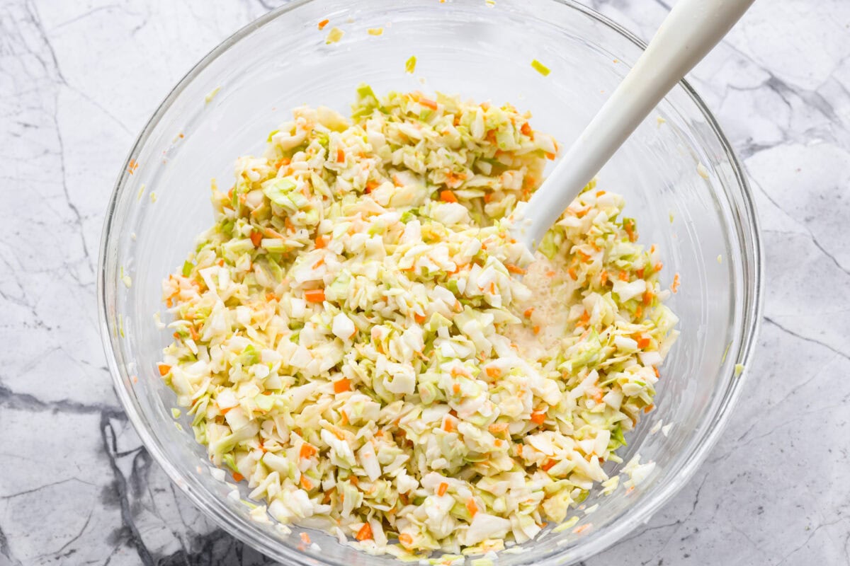 My Copycat KFC Coleslaw is so spot-on, you’ll think it’s the real deal! Crunchy, creamy, tangy, and perfect for any BBQ, everyone will want the recipe! Cabbage mixture and dressing being stirred together.
