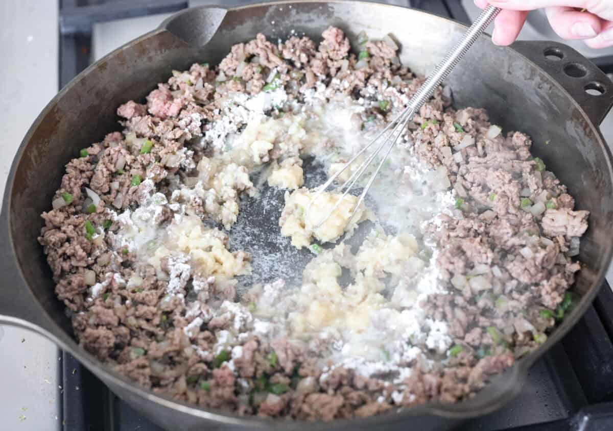 Creamy, cheesy Cowboy Mac and Cheese gets a bold twist with hearty additions like seasoned meat, tomatoes, jalapeños, corn, beans, and onions. It's rich, flavorful, and just the right amount of spice! The heat is warm but not overwhelming. If you like it spicy, add more jalapeños! Butter and flour being whisked into the ground beef mixture.