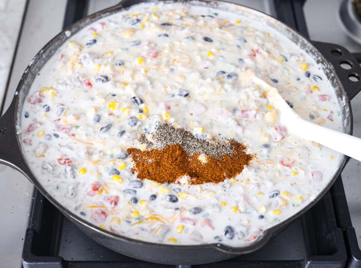 Creamy, cheesy Cowboy Mac and Cheese gets a bold twist with hearty additions like seasoned meat, tomatoes, jalapeños, corn, beans, and onions. It's rich, flavorful, and just the right amount of spice! The heat is warm but not overwhelming. If you like it spicy, add more jalapeños! Overhead shot of the cheese, chili powder and salt and pepper added to the mixture.