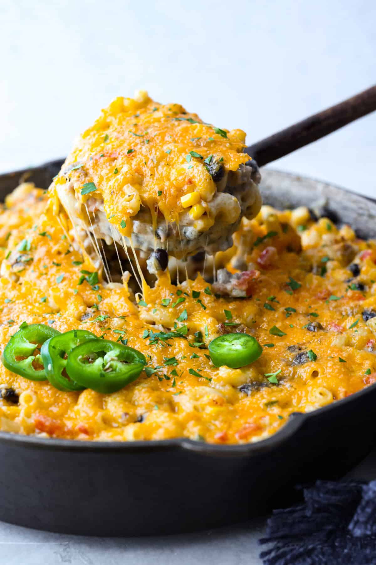 Creamy, cheesy Cowboy Mac and Cheese gets a bold twist with hearty additions like seasoned meat, tomatoes, jalapeños, corn, beans, and onions. It's rich, flavorful, and just the right amount of spice! The heat is warm but not overwhelming. If you like it spicy, add more jalapeños! Close up shot of someone pulling a scoop of cowboy mac and cheese out of the skillet.