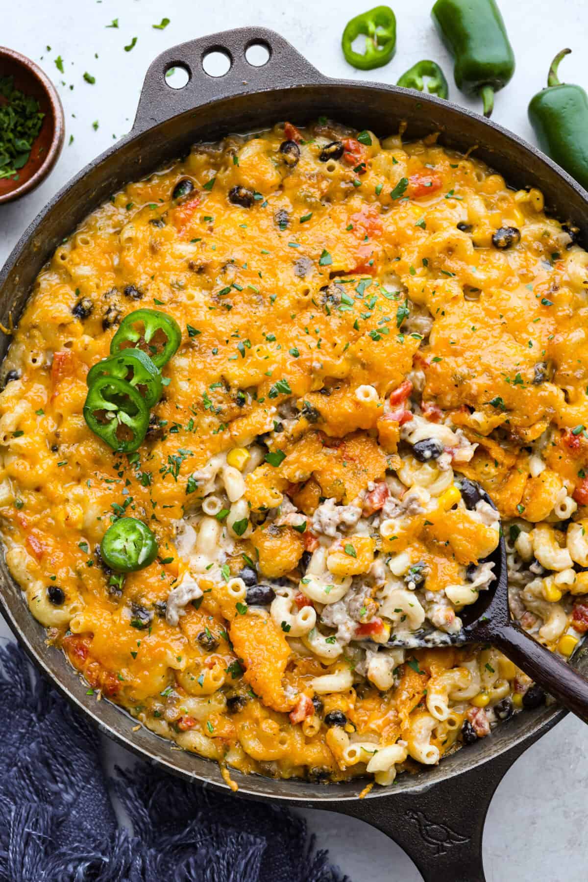 Creamy, cheesy Cowboy Mac and Cheese gets a bold twist with hearty additions like seasoned meat, tomatoes, jalapeños, corn, beans, and onions. It's rich, flavorful, and just the right amount of spice! The heat is warm but not overwhelming. If you like it spicy, add more jalapeños! Tops down shot of cowboy mac and cheese in a skillet, garnished with sliced jalapeño.