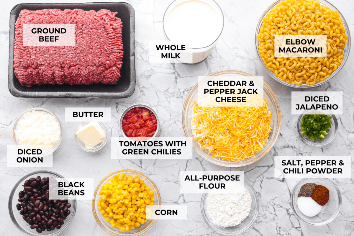 Creamy, cheesy Cowboy Mac and Cheese gets a bold twist with hearty additions like seasoned meat, tomatoes, jalapeños, corn, beans, and onions. It's rich, flavorful, and just the right amount of spice! The heat is warm but not overwhelming. If you like it spicy, add more jalapeños! Overhead shot of labeled cowboy mac and cheese ingredients.