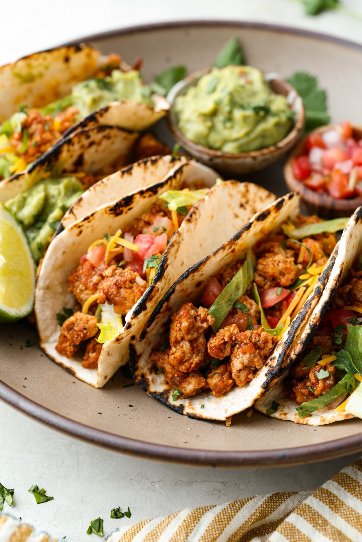 These ground turkey tacos are full of fiesta flavor, all with less fat! Don't let ground turkey steer you away! No one will miss the beef once they taste this taco filling. The seasonings and flavors absorb perfectly into the meat. Angle shot of ground turkey tacos on a serving plate.