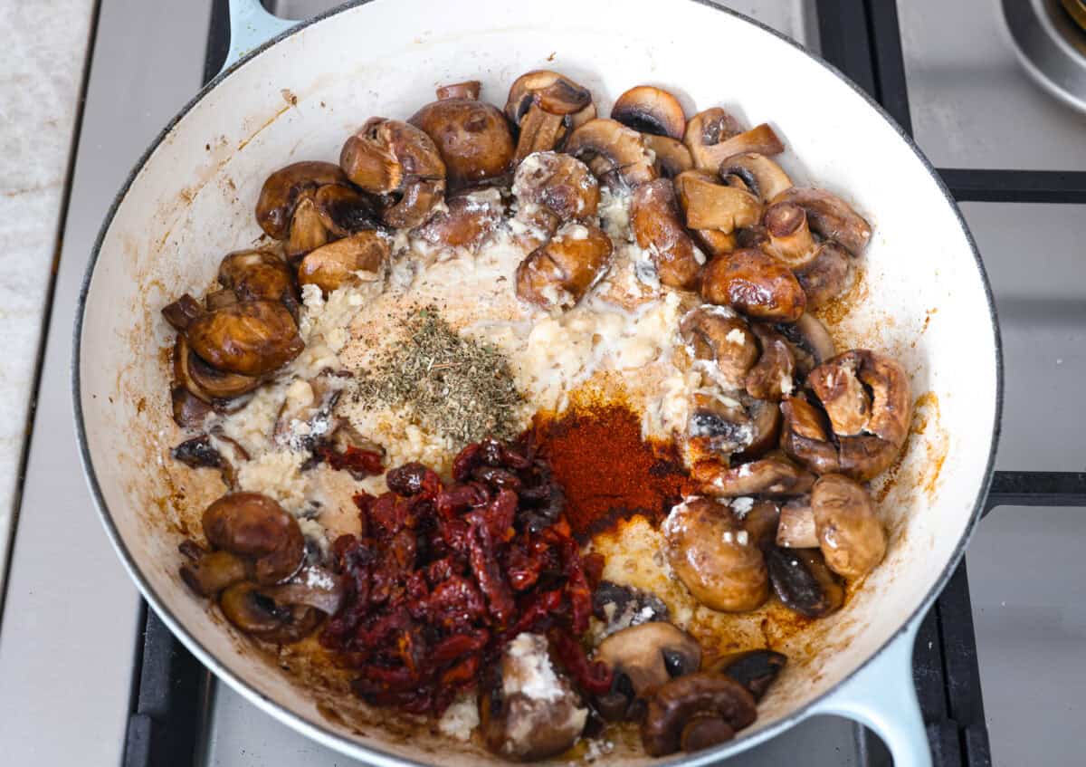 The key to making these Marry Me Mushrooms irresistibly flavorful is getting the perfect sear on the mushrooms. This locks in their natural flavors and texture. Then they simmer in a creamy garlic parmesan sauce with robust sun-dried tomatoes and herbs. It’s a simple technique that makes all the difference! Overhead shot of the seasonings and sun-dried tomatoes adde in with the mushrooms and flour in a skillet.