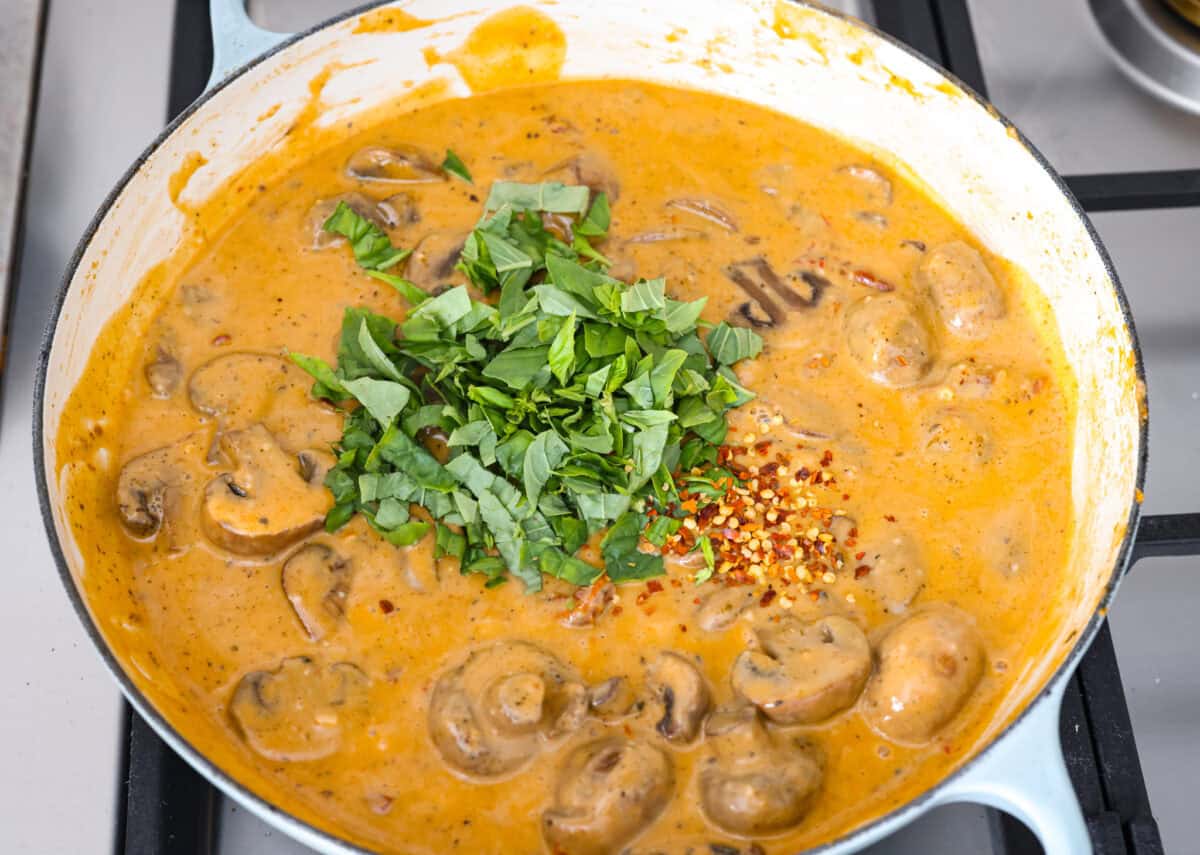 The key to making these Marry Me Mushrooms irresistibly flavorful is getting the perfect sear on the mushrooms. This locks in their natural flavors and texture. Then they simmer in a creamy garlic parmesan sauce with robust sun-dried tomatoes and herbs. It’s a simple technique that makes all the difference! Overhead shot of chopped basil leaves and red pepper flakes added to the sauce.