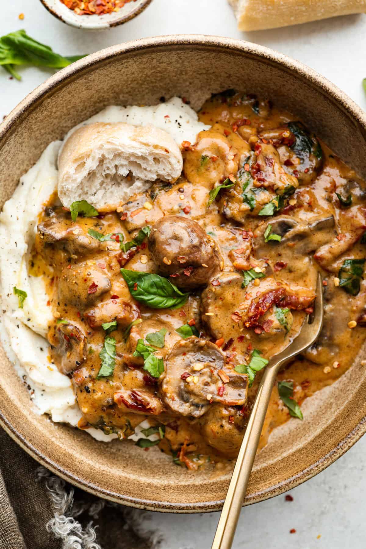 The key to making these Marry Me Mushrooms irresistibly flavorful is getting the perfect sear on the mushrooms. This locks in their natural flavors and texture. Then they simmer in a creamy garlic parmesan sauce with robust sun-dried tomatoes and herbs. It’s a simple technique that makes all the difference! Overhead shot of plated marry me mushrooms over mashed potatoes and a crust of bread.