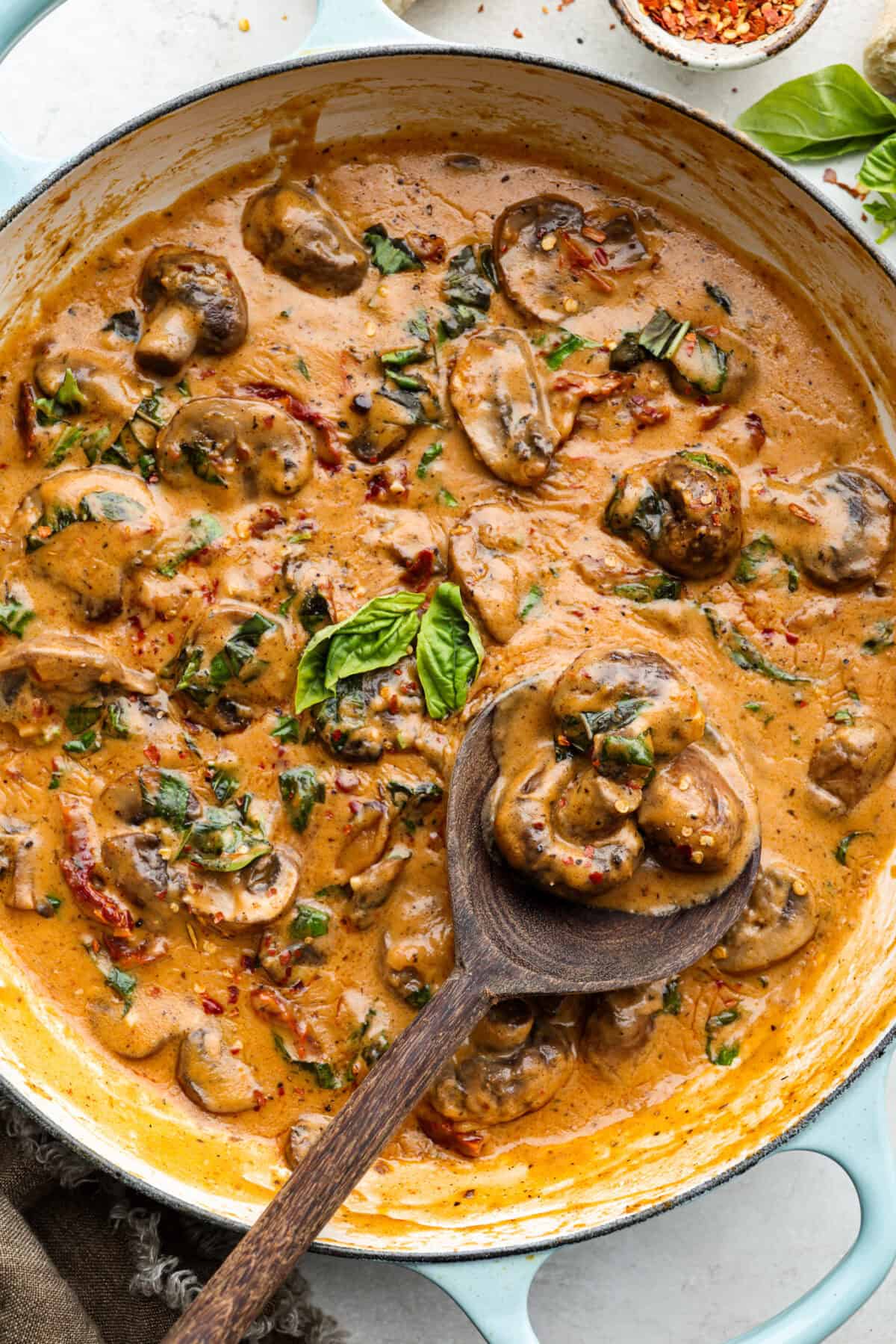 The key to making these Marry Me Mushrooms irresistibly flavorful is getting the perfect sear on the mushrooms. This locks in their natural flavors and texture. Then they simmer in a creamy garlic parmesan sauce with robust sun-dried tomatoes and herbs. It’s a simple technique that makes all the difference! Marry Me mushroom sauce in a skillet with wooden serving spoon scooping out a spoonful.