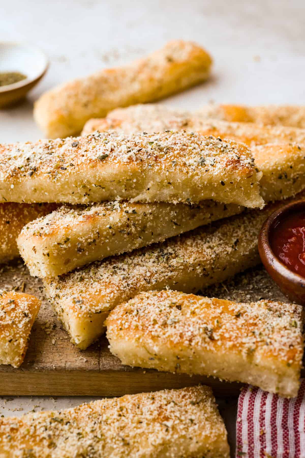 Pile of Pizza Hut breadsticks on a cutting board with a bowl of marinara sauce next to them.
