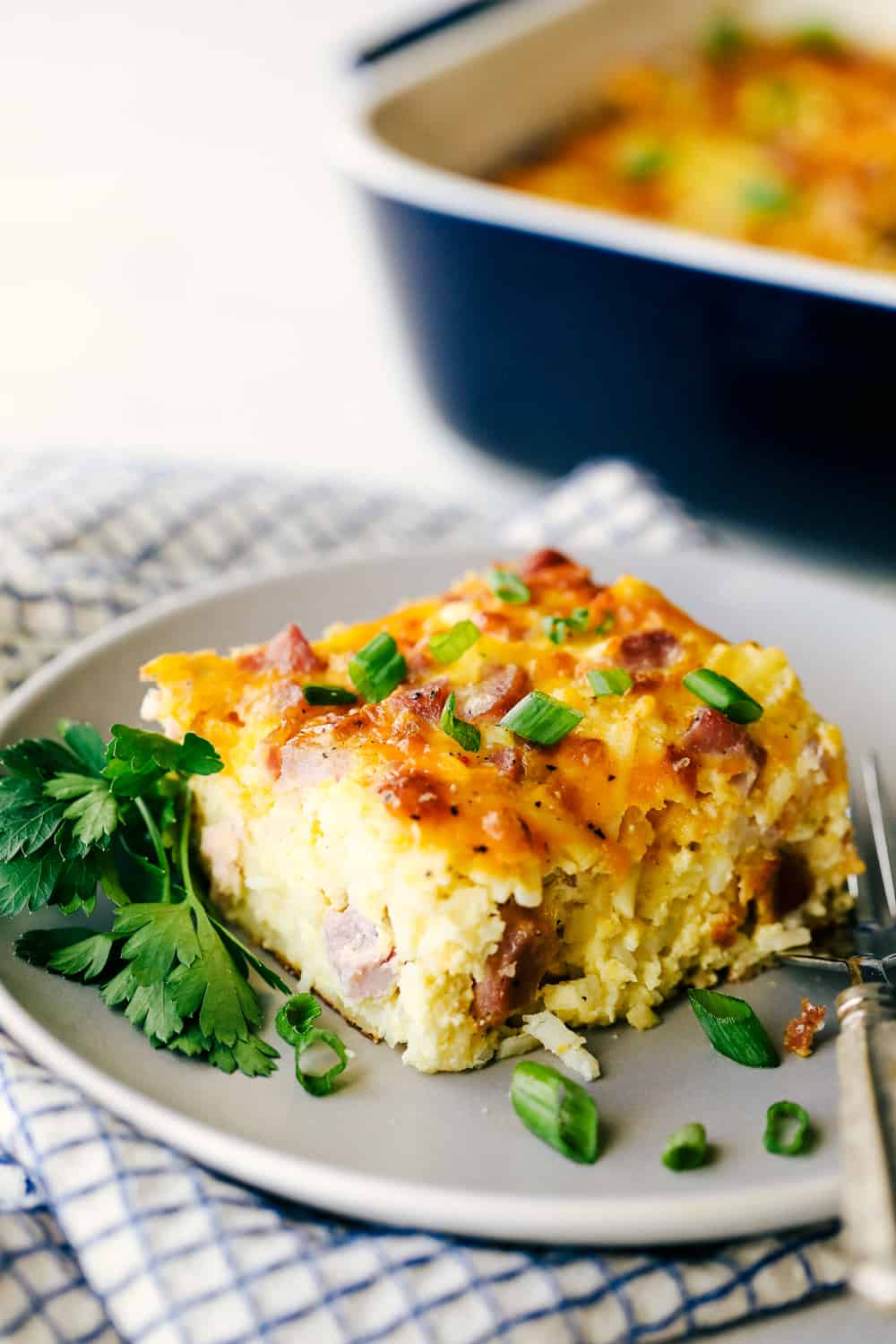 The Best Breakfast Casserole is a thick and creamy egg base with shredded potatoes, chunks of ham and flavorful cheese blends that bakes up in no time. Make ahead or enjoy the morning of during the holidays! Angle shot of a plated slice of casserole.